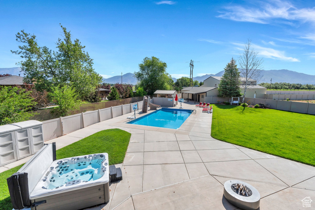 View of pool with a water slide, a mountain view, a patio, and a hot tub