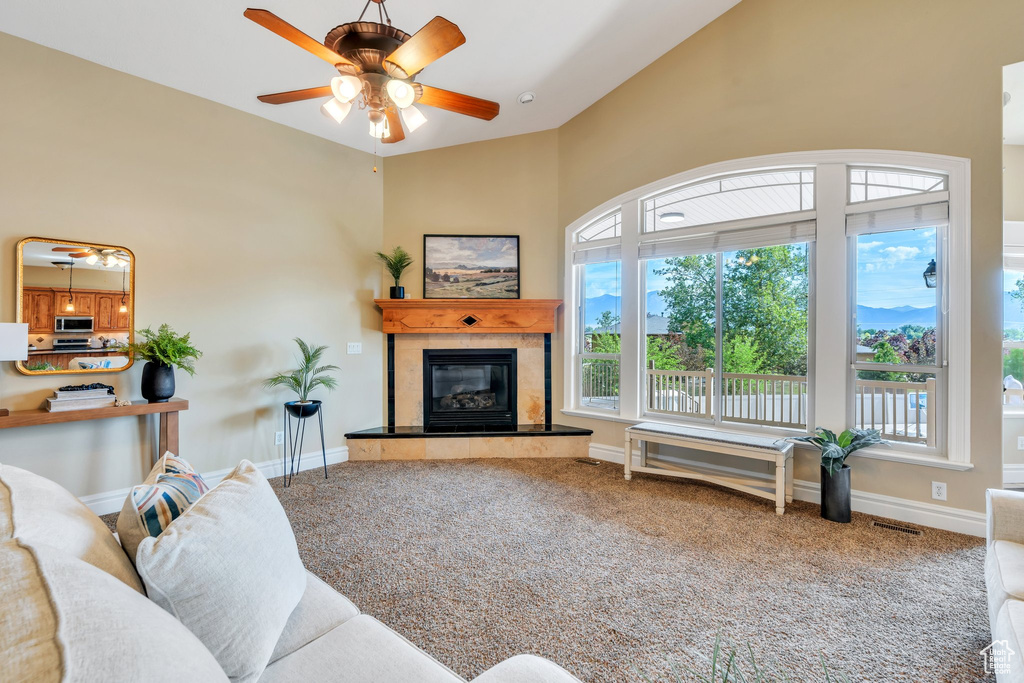 Carpeted living room featuring a tiled fireplace, ceiling fan, high vaulted ceiling, and baseboards