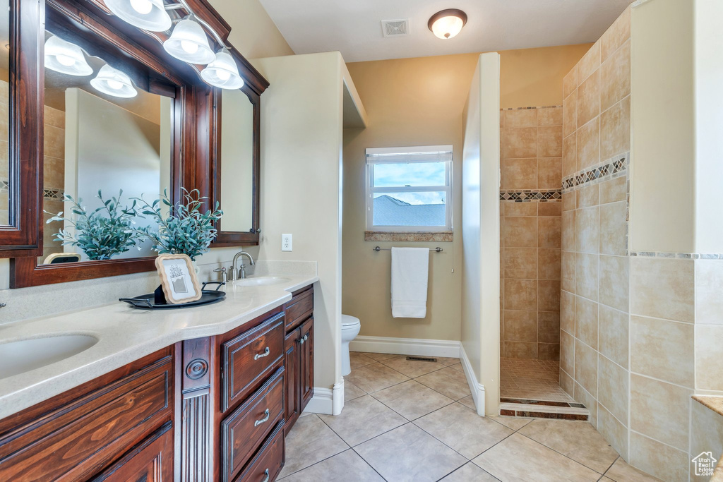 Full bathroom with double vanity, toilet, tile patterned floors, a tile shower, and baseboards