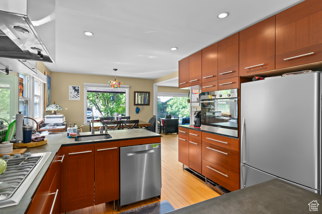 Kitchen with appliances with stainless steel finishes, a sink, ventilation hood, a peninsula, and light wood finished floors
