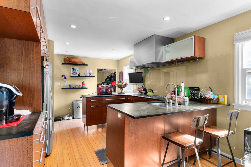 Kitchen featuring a sink, a peninsula, dark countertops, a breakfast bar area, and light wood-style flooring