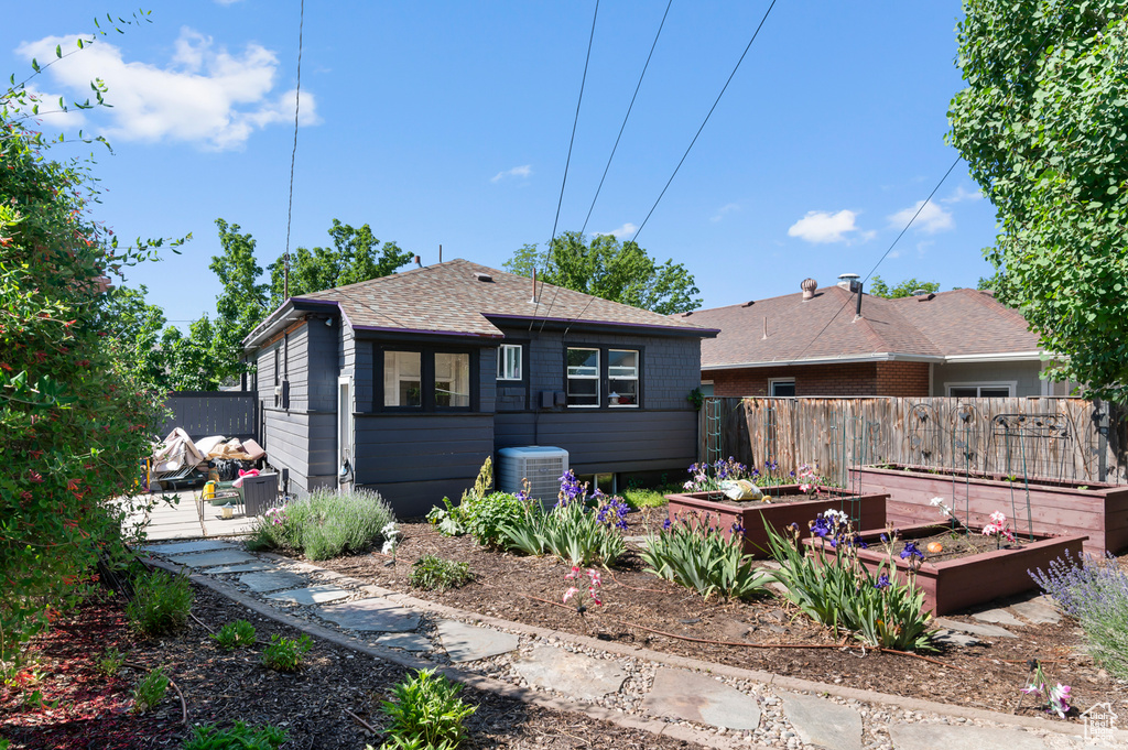 Rear view of house featuring a garden, roof with shingles, and central AC