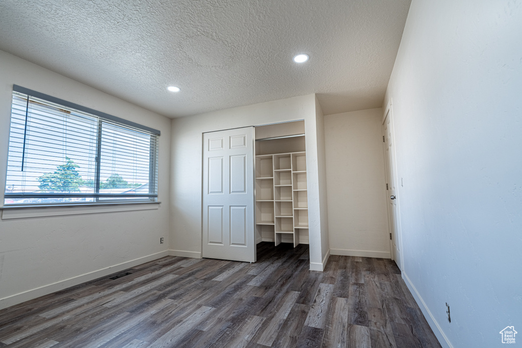 Unfurnished bedroom featuring a textured ceiling, wood finished floors, a closet, baseboards, and recessed lighting