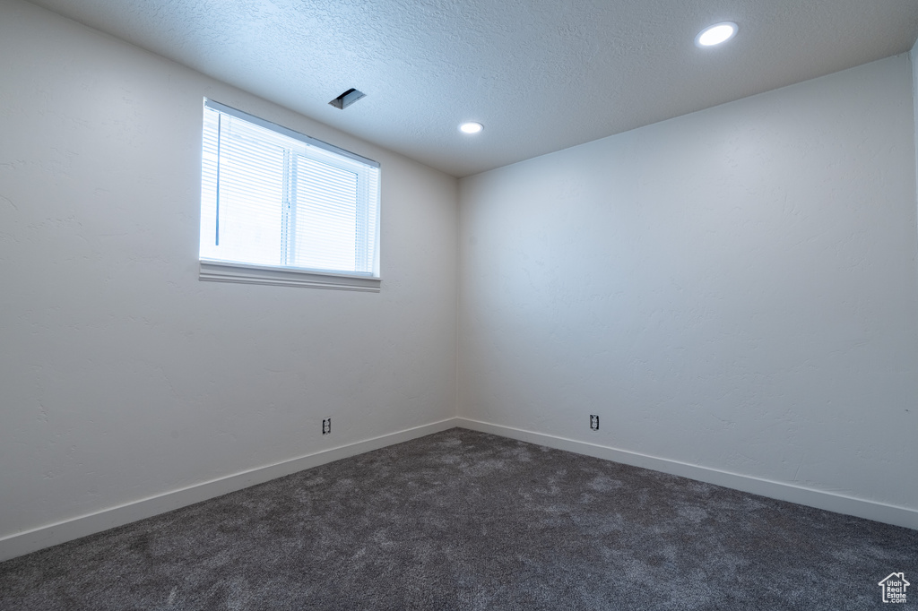 Empty room featuring dark carpet, recessed lighting, baseboards, and a textured ceiling