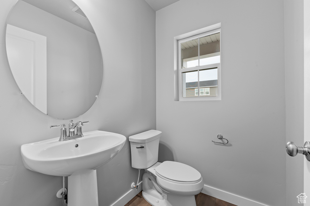 Bathroom featuring baseboards, wood finished floors, toilet, and a sink
