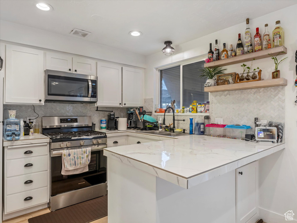 Kitchen featuring stainless steel appliances, a sink, a peninsula, white cabinetry, and decorative backsplash