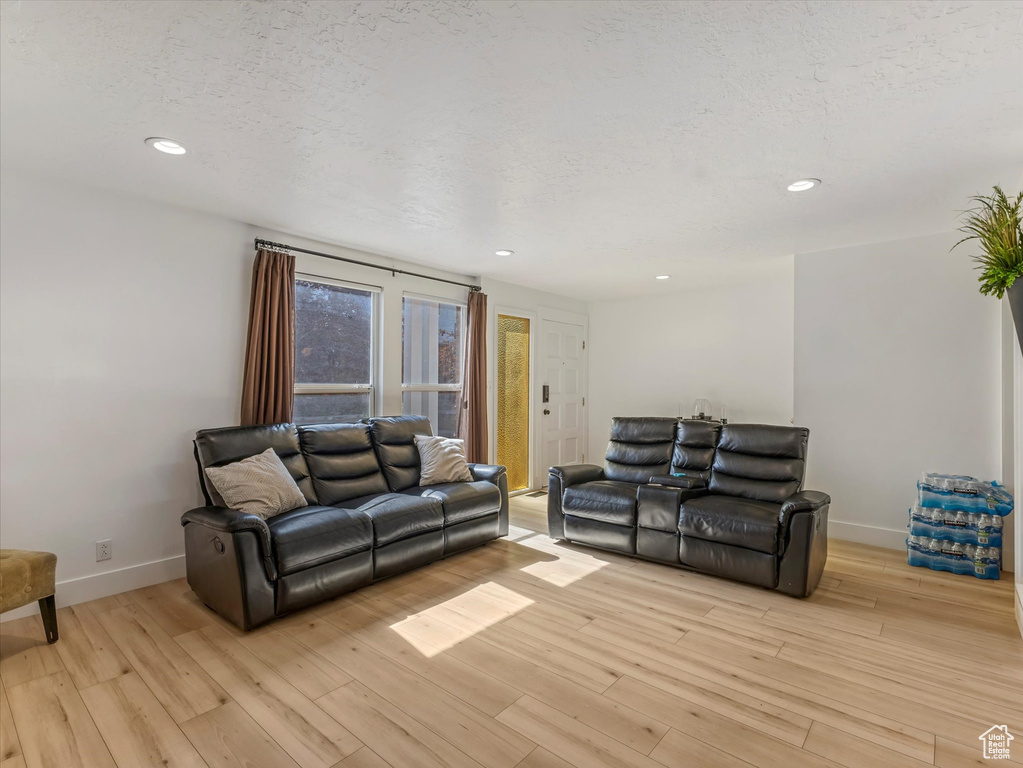 Living room featuring light wood finished floors, baseboards, recessed lighting, and a textured ceiling