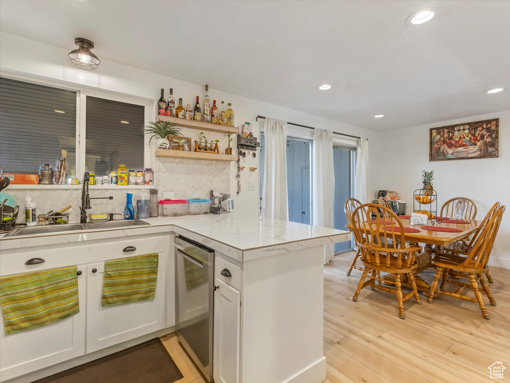 Kitchen with stainless steel dishwasher, a sink, light countertops, a peninsula, and tasteful backsplash