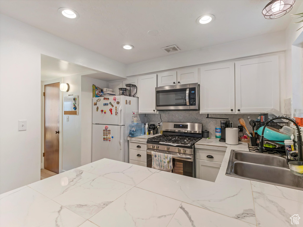 Kitchen featuring stainless steel appliances, a sink, decorative backsplash, white cabinets, and light stone countertops