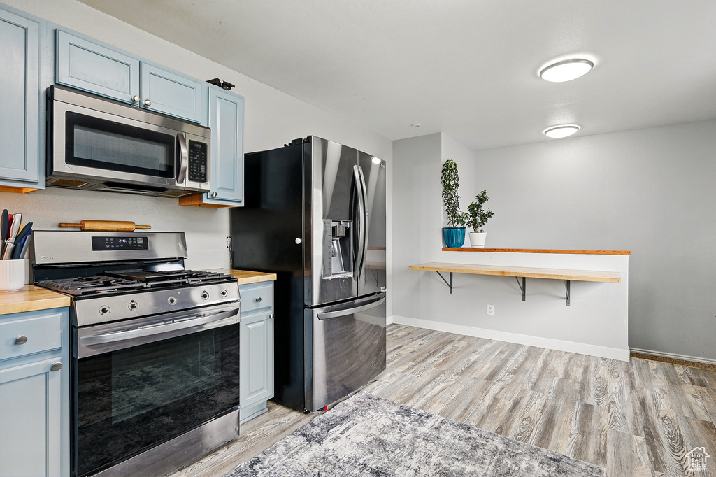 Kitchen with stainless steel appliances, butcher block countertops, light wood-style flooring, and baseboards