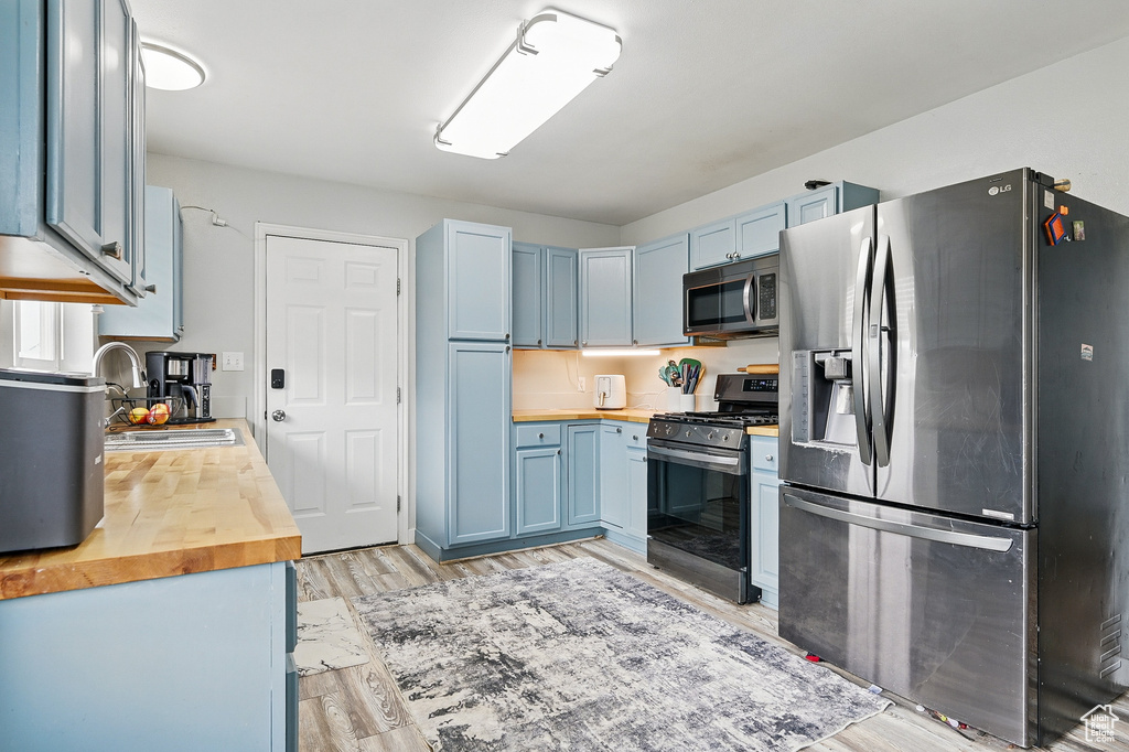 Kitchen featuring appliances with stainless steel finishes, butcher block countertops, blue cabinets, and a sink