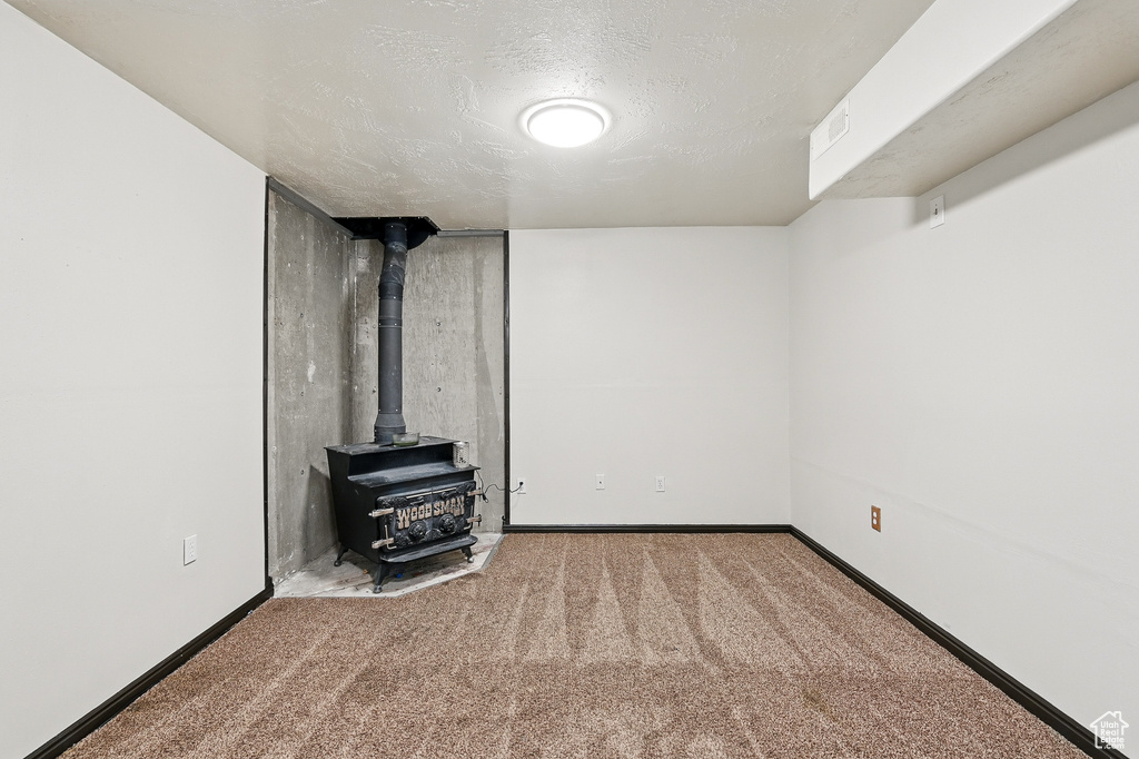 Finished below grade area with a wood stove, carpet flooring, baseboards, and a textured ceiling