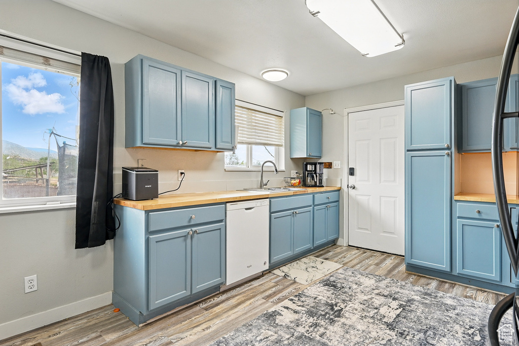 Kitchen featuring dishwasher, blue cabinetry, wooden counters, and a sink