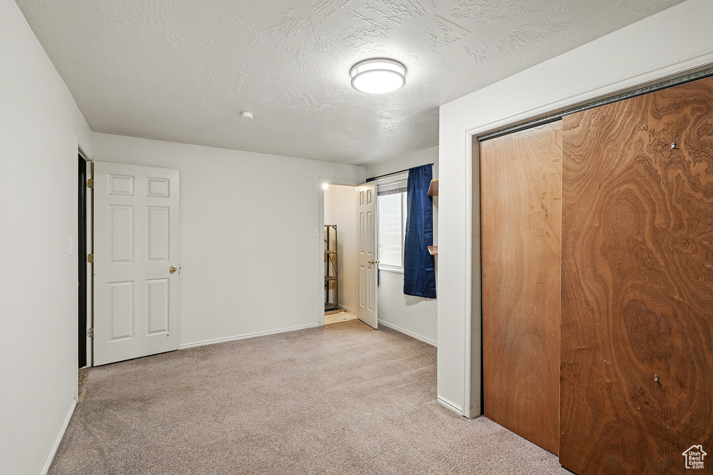 Unfurnished bedroom with light carpet, baseboards, a closet, and a textured ceiling