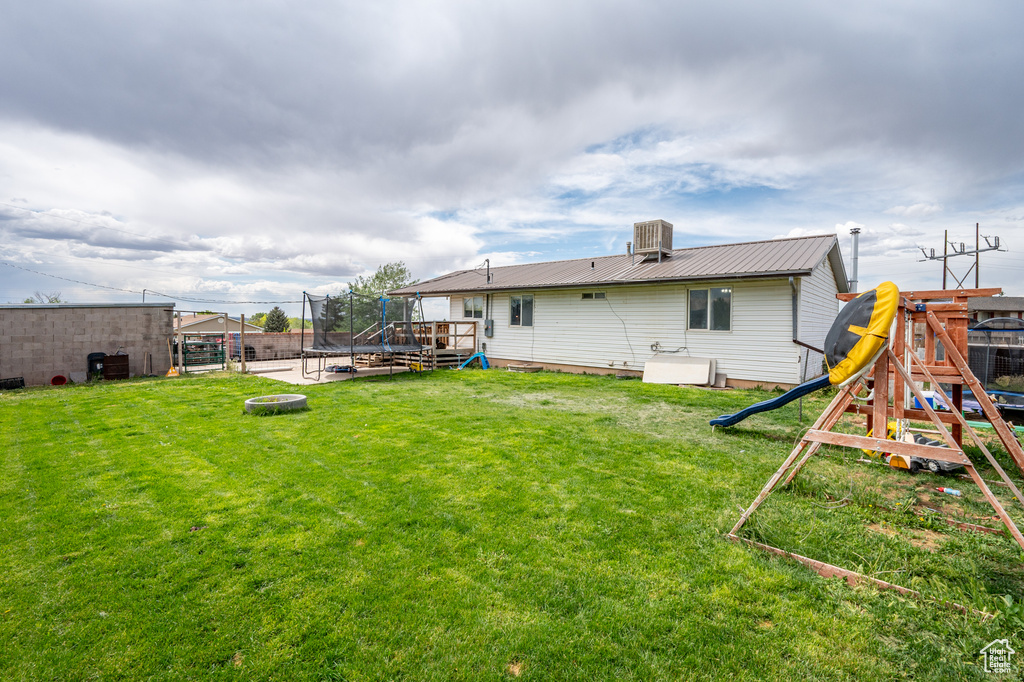 Back of property featuring a trampoline, a playground, metal roof, central AC unit, and a deck
