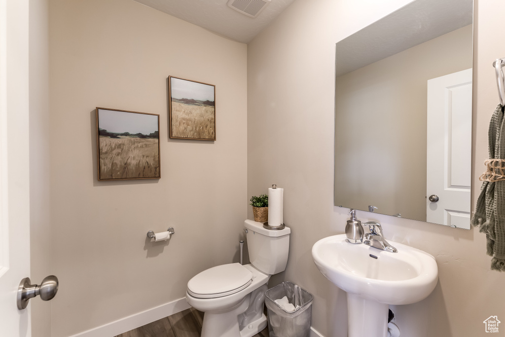 Bathroom featuring toilet, wood finished floors, baseboards, and a sink