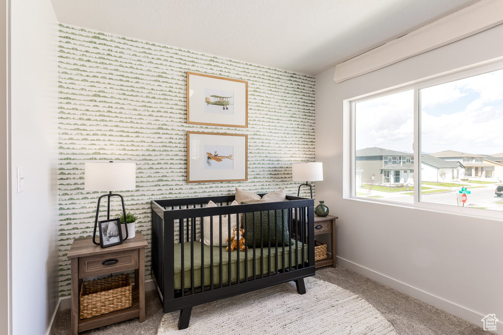Carpeted bedroom with baseboards, multiple windows, wallpapered walls, a crib, and an accent wall