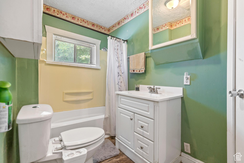 Full bath featuring toilet, a textured ceiling, vanity, and shower / bath combo