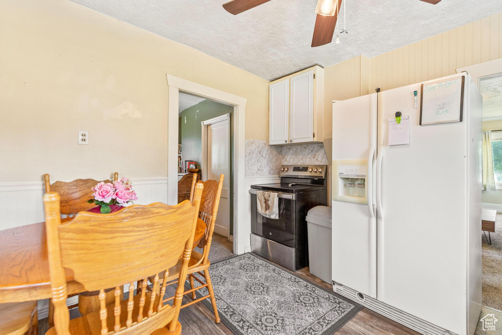 Kitchen with stainless steel range with electric cooktop, white fridge with ice dispenser, a ceiling fan, a textured ceiling, and wainscoting