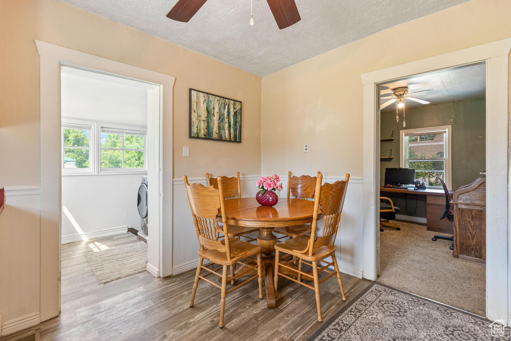 Dining space featuring ceiling fan, a textured ceiling, wood finished floors, an office area, and wainscoting