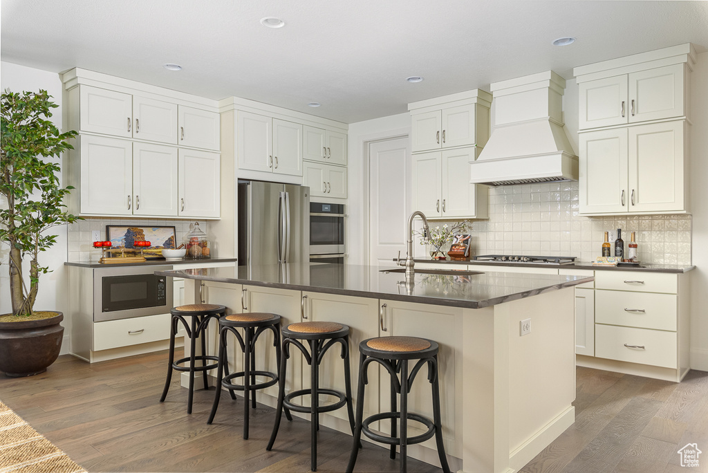 Kitchen featuring a sink, premium range hood, stainless steel appliances, dark countertops, and wood finished floors