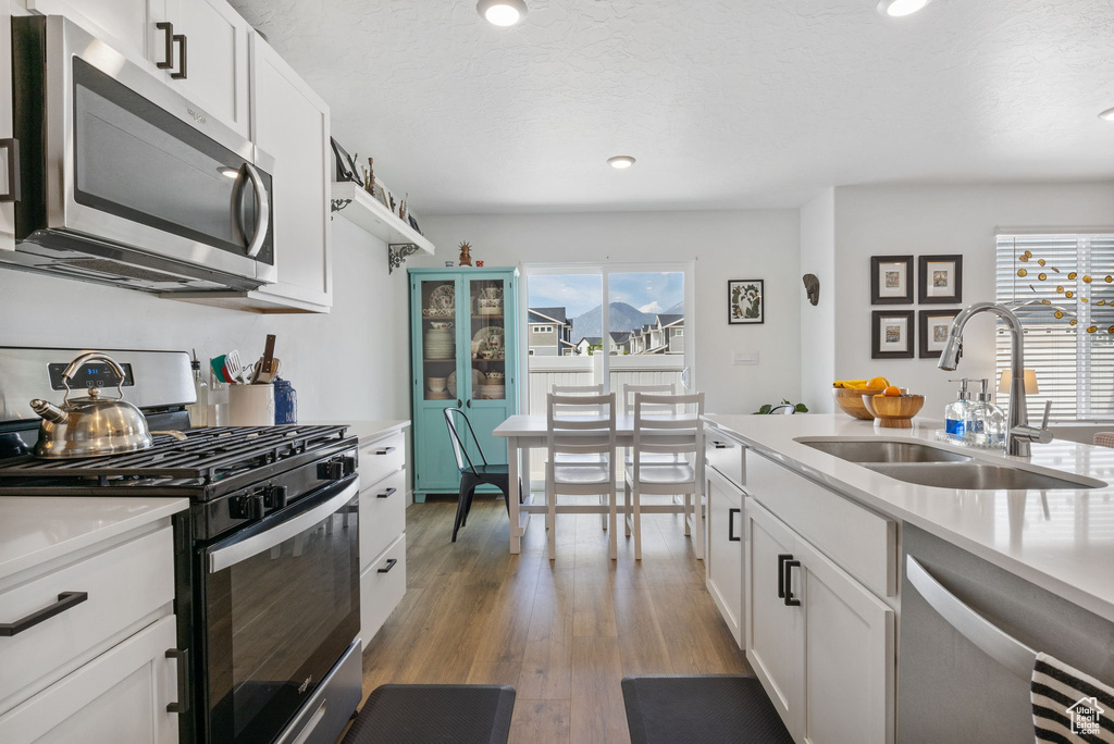 Kitchen with appliances with stainless steel finishes, a sink, light countertops, white cabinets, and recessed lighting