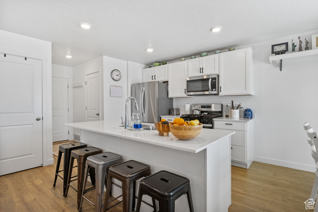 Kitchen featuring appliances with stainless steel finishes, light wood-style floors, a breakfast bar area, white cabinets, and recessed lighting
