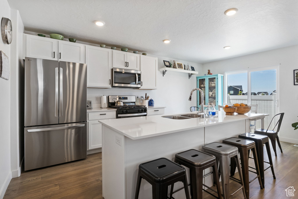 Kitchen featuring stainless steel appliances, a sink, dark wood-type flooring, a kitchen bar, and white cabinetry