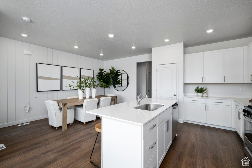 Kitchen featuring a sink, appliances with stainless steel finishes, dark wood-type flooring, light countertops, and white cabinets