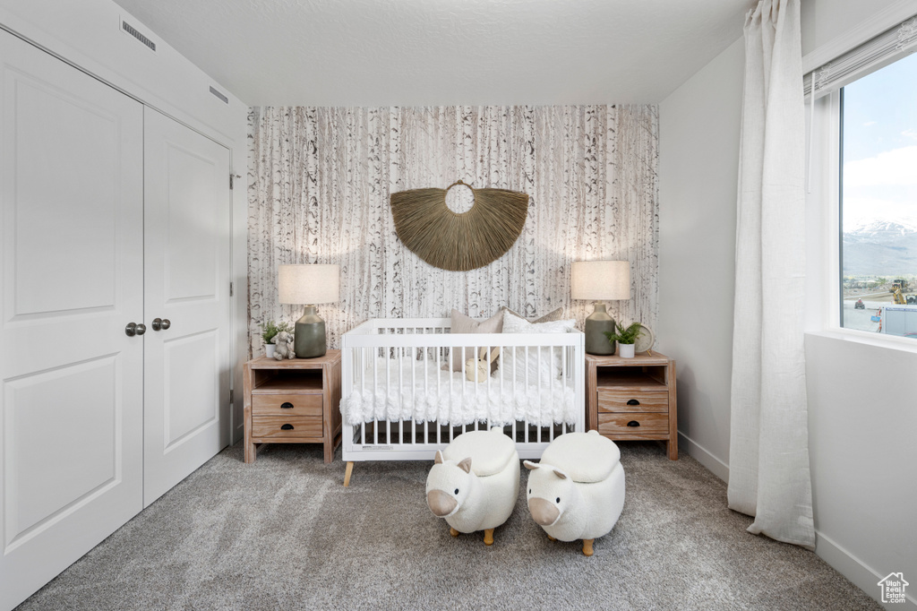 Carpeted bedroom with multiple windows, a crib, a closet, and baseboards