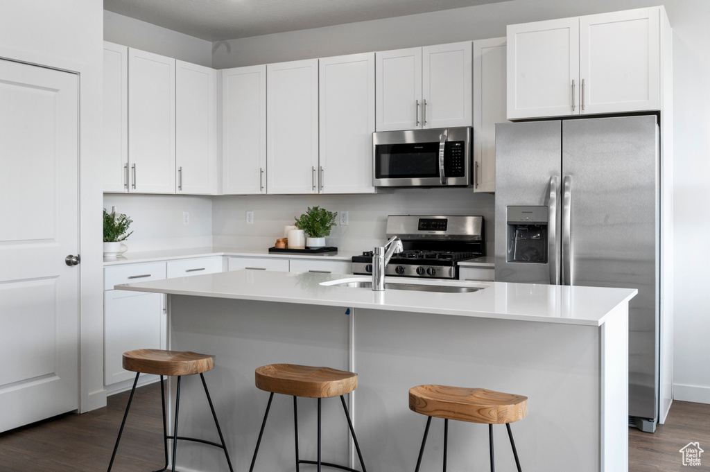 Kitchen with stainless steel appliances, a sink, dark wood finished floors, white cabinets, and a breakfast bar