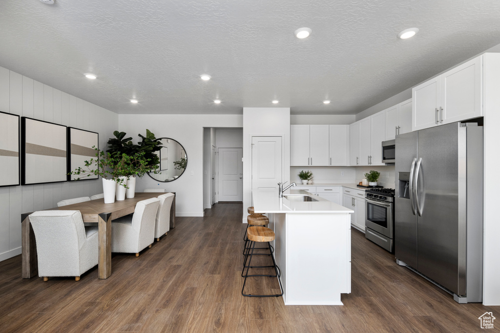 Kitchen featuring stainless steel appliances, a sink, dark wood-type flooring, a breakfast bar area, and light countertops