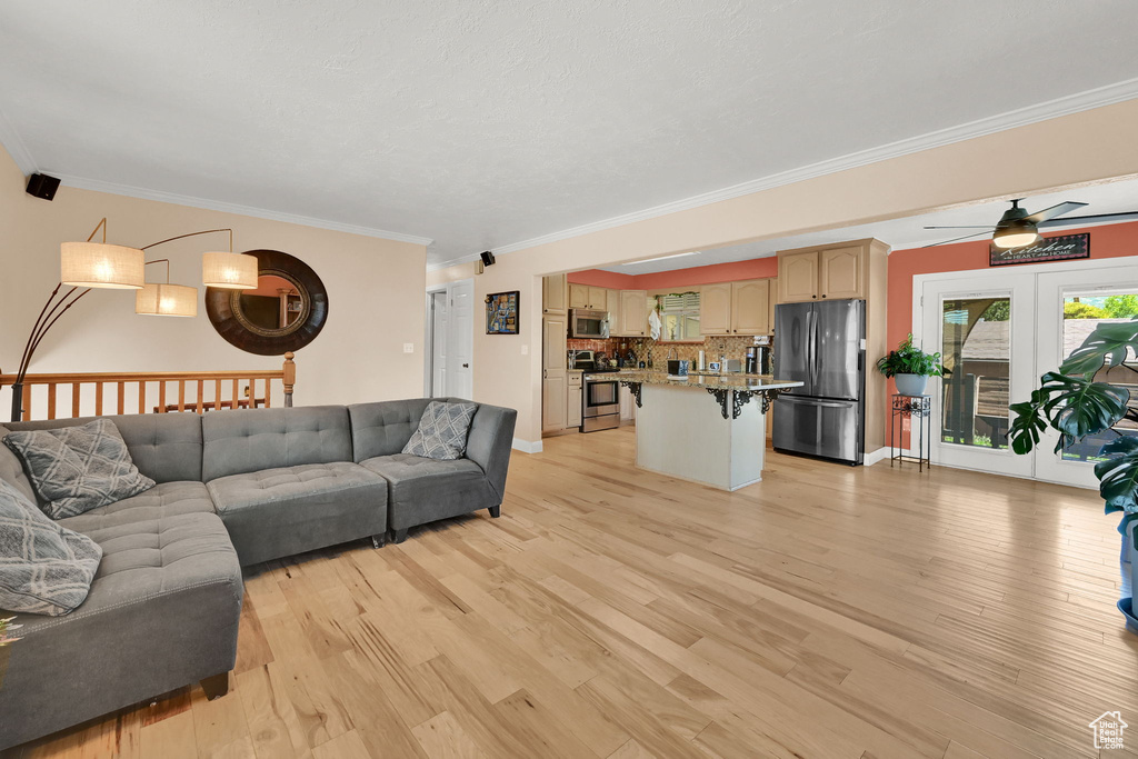 Living room with ornamental molding, light wood-style flooring, a ceiling fan, and baseboards