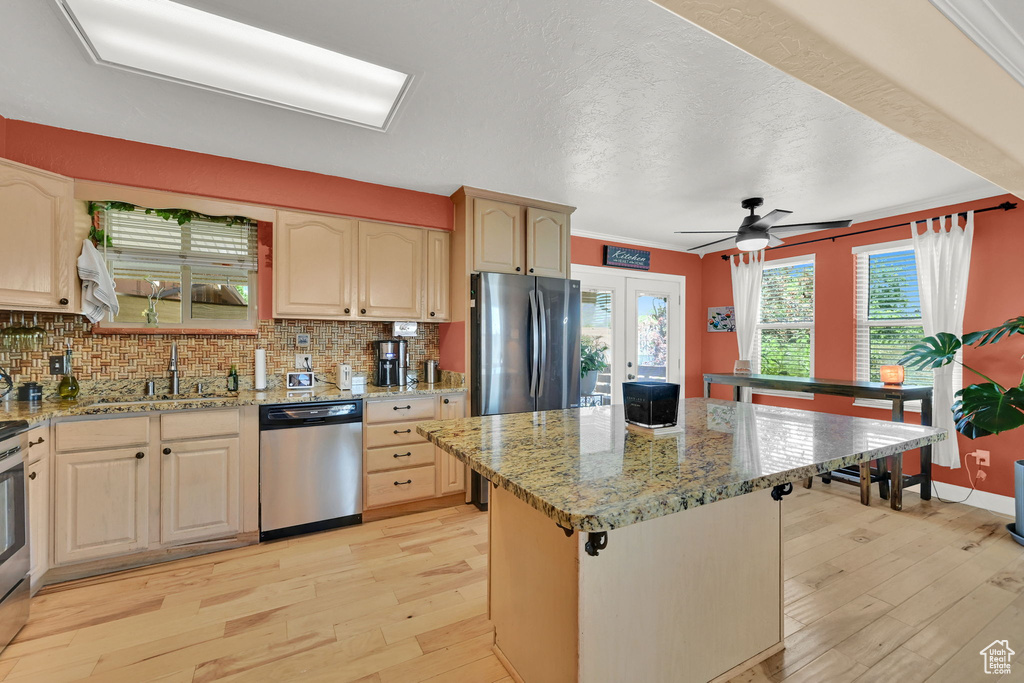 Kitchen featuring stainless steel appliances, light wood finished floors, backsplash, a kitchen island, and a textured ceiling
