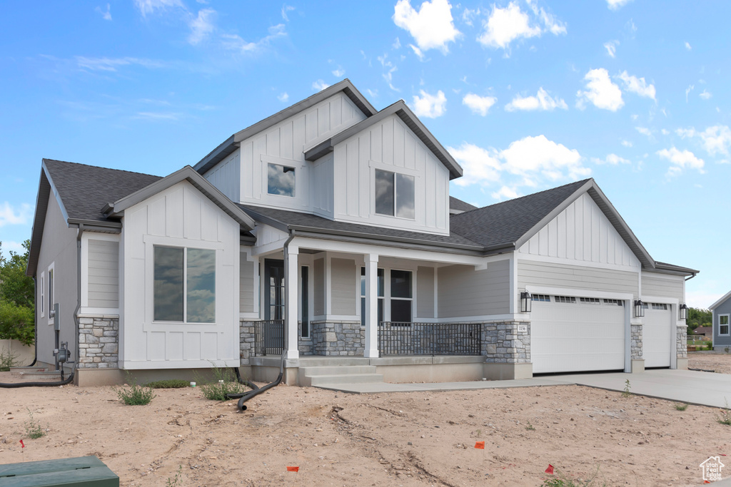 View of front of house with board and batten siding, a porch, stone siding, and an attached garage