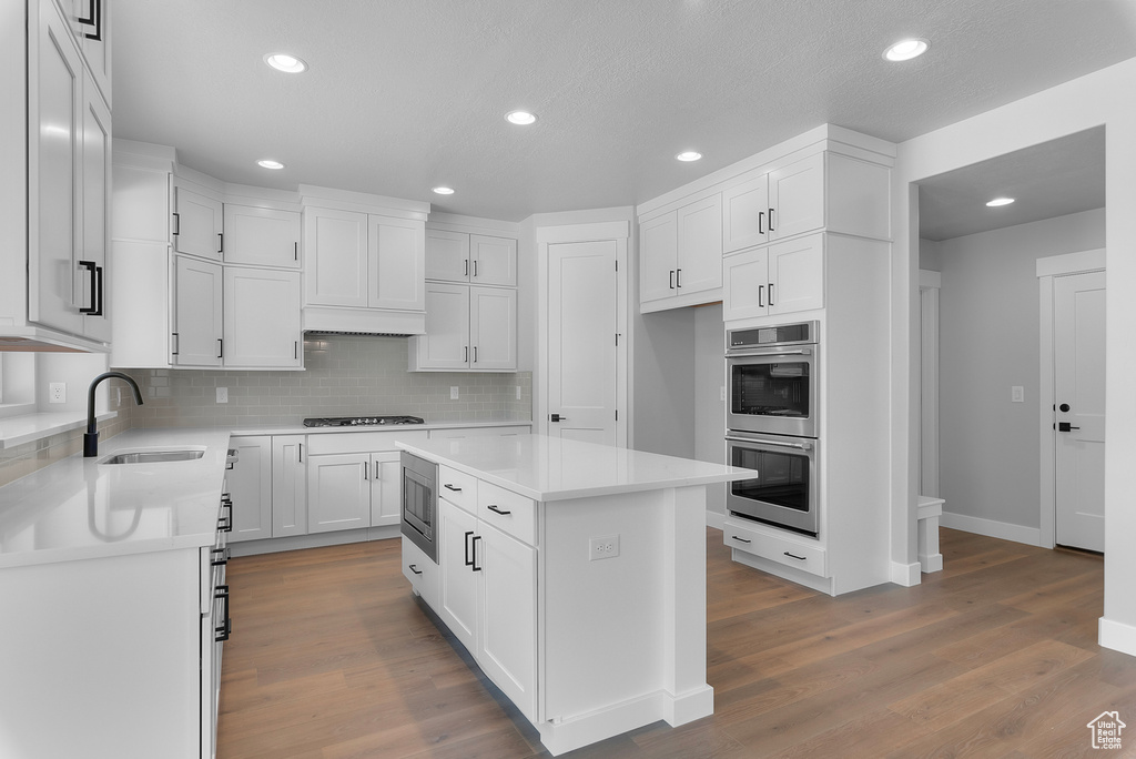 Kitchen with a sink, stainless steel appliances, recessed lighting, decorative backsplash, and white cabinetry