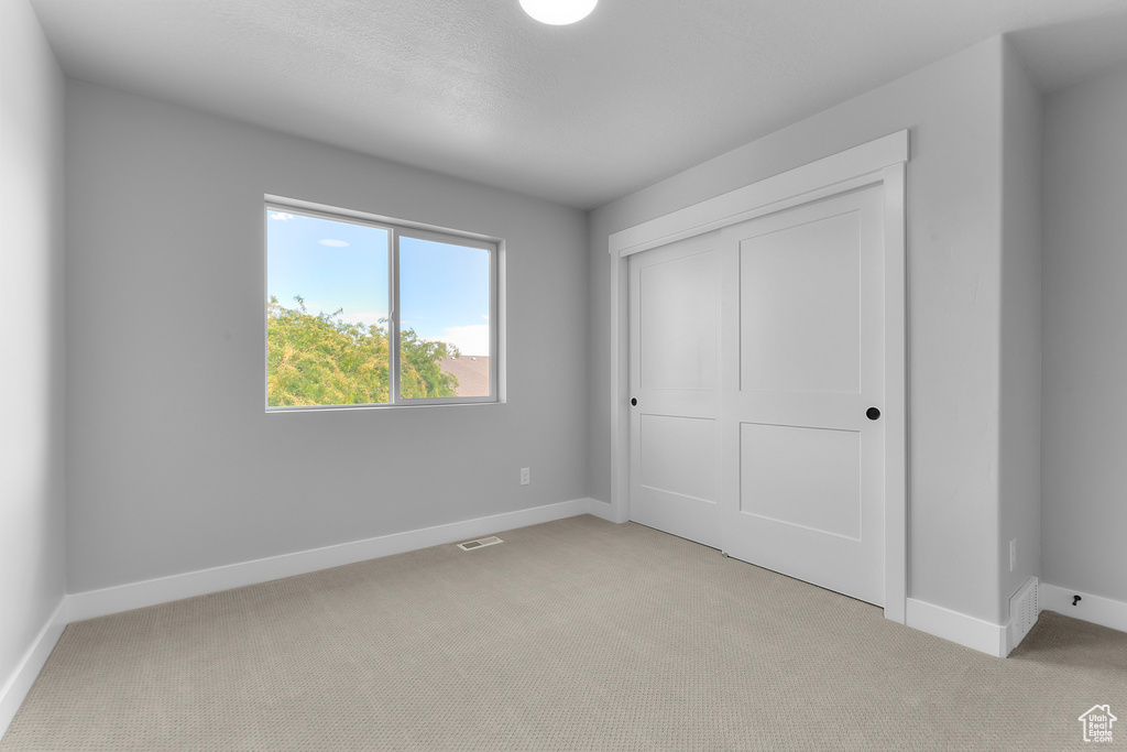 Unfurnished bedroom featuring light carpet, baseboards, and a closet
