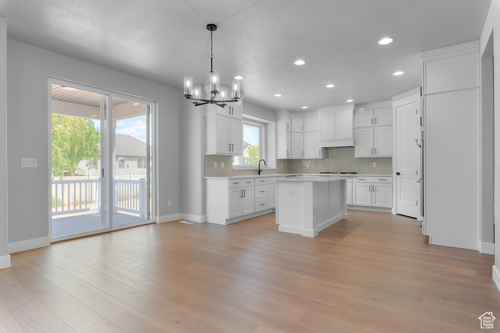 Kitchen with a chandelier, light countertops, tasteful backsplash, white cabinets, and a kitchen island