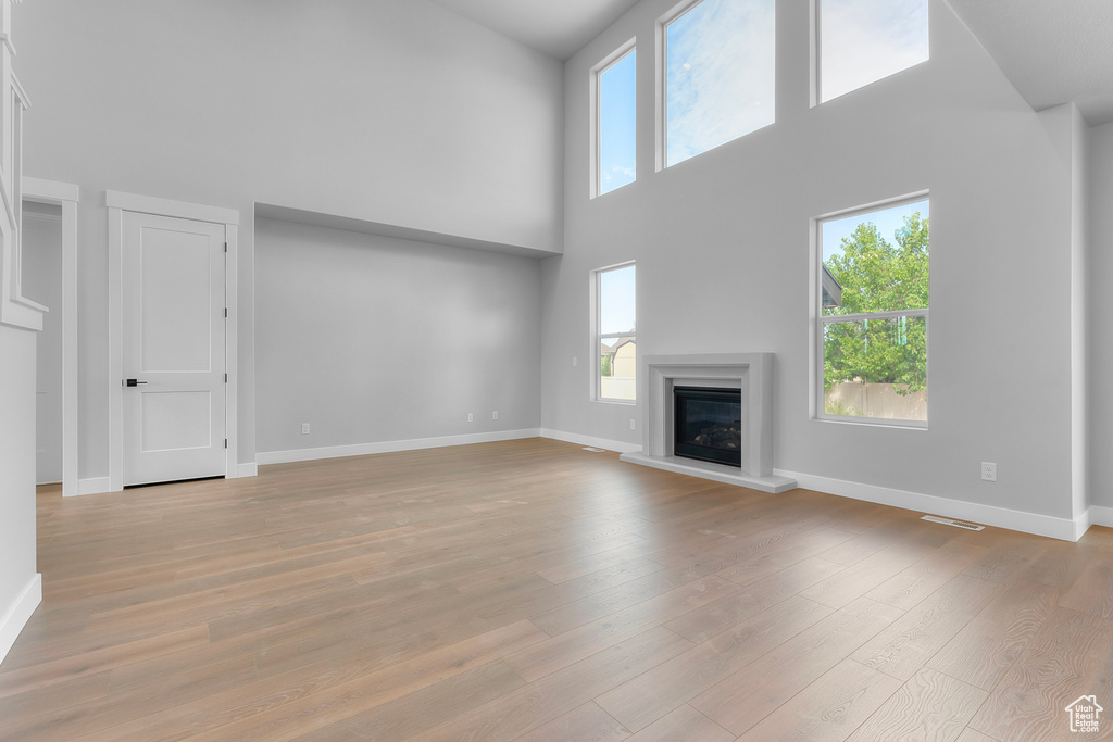Unfurnished living room featuring a high ceiling, baseboards, a glass covered fireplace, and light wood-style floors
