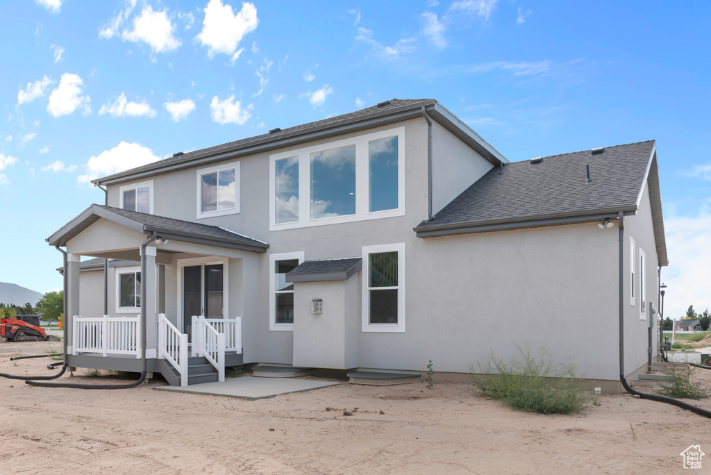Back of property featuring a shingled roof and stucco siding