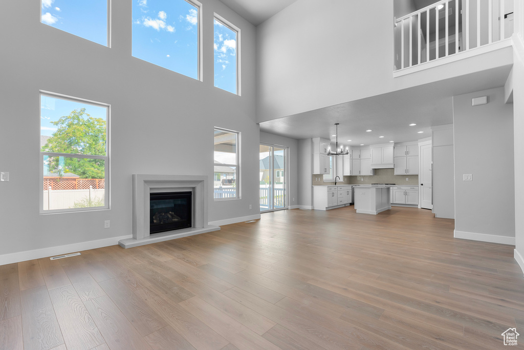 Unfurnished living room with a high ceiling, a sink, a chandelier, baseboards, and plenty of natural light