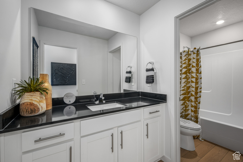 Bathroom with toilet, vanity, wood finished floors, and shower / tub combo with curtain