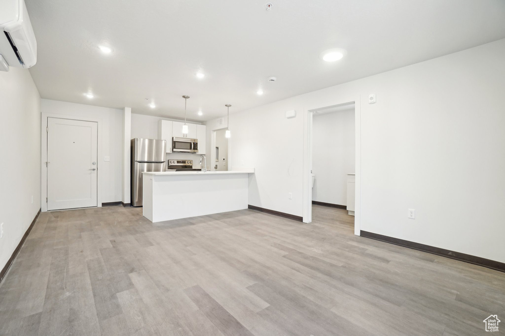 Unfurnished living room featuring light wood finished floors, a wall unit AC, recessed lighting, and baseboards