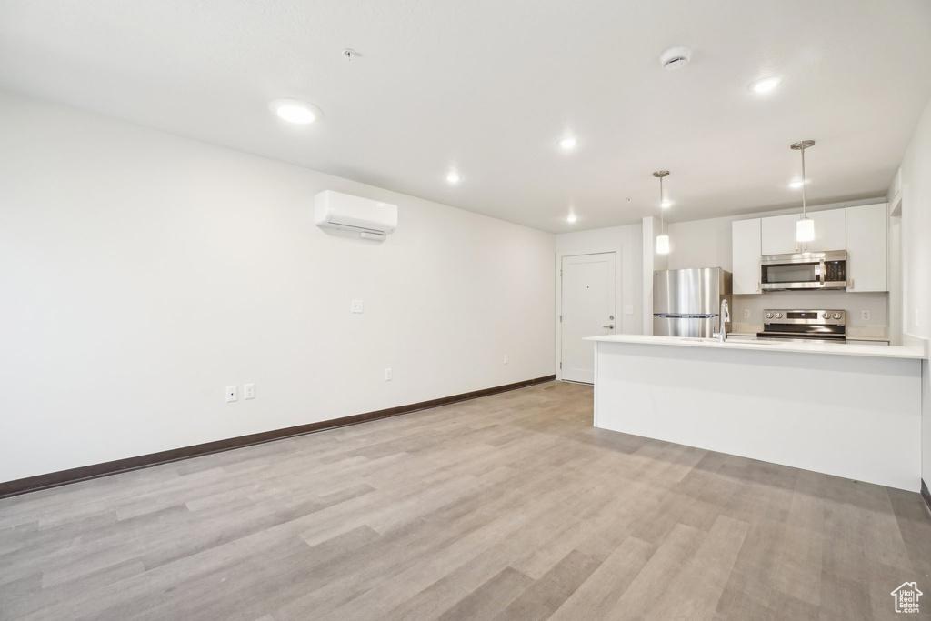 Unfurnished living room featuring light wood-style flooring, an AC wall unit, recessed lighting, and baseboards