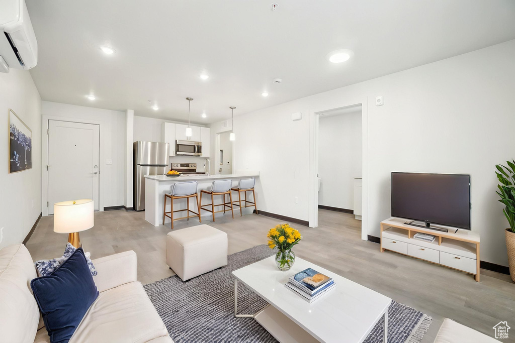 Living room with light wood-style flooring, an AC wall unit, recessed lighting, and baseboards