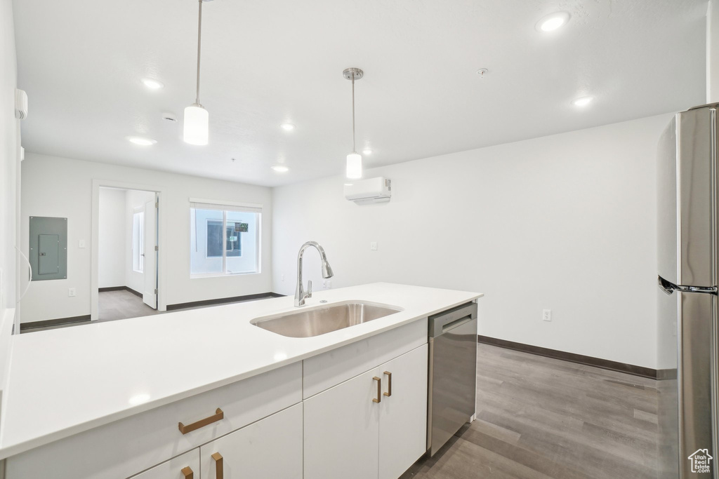Kitchen with a sink, electric panel, stainless steel appliances, light countertops, and wood finished floors