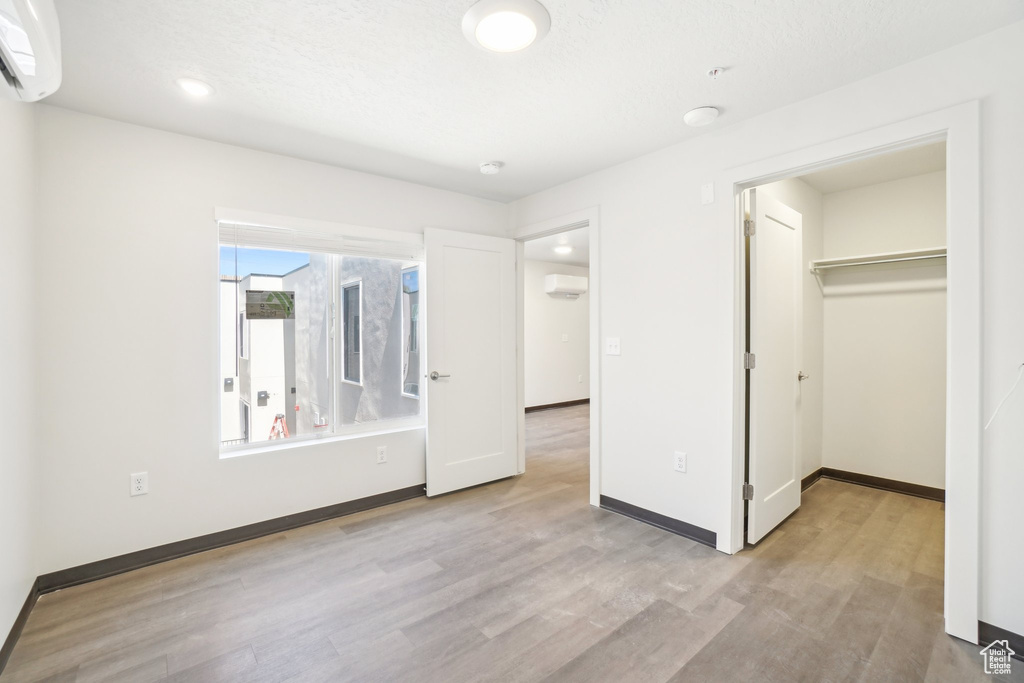 Unfurnished bedroom with wood finished floors, a wall unit AC, baseboards, a spacious closet, and recessed lighting