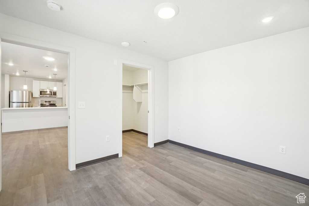 Unfurnished bedroom featuring freestanding refrigerator, light wood-style flooring, baseboards, a spacious closet, and a closet