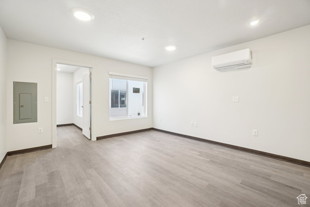 Empty room with electric panel, an AC wall unit, light wood-style floors, baseboards, and recessed lighting