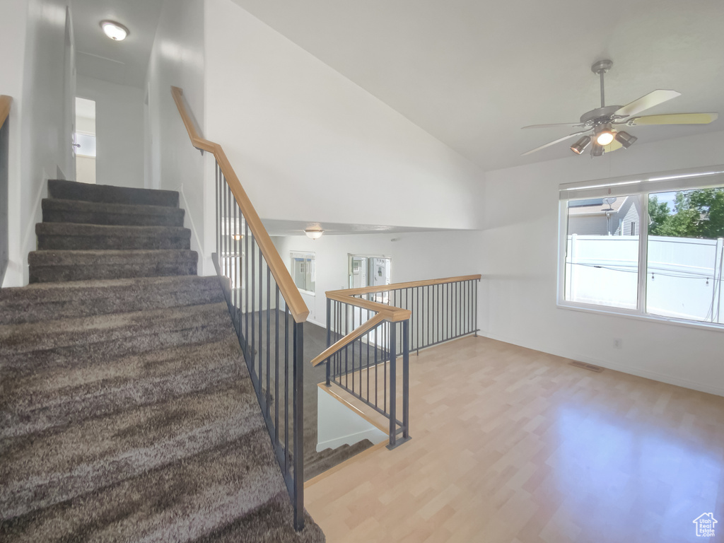 Stairway with a ceiling fan, vaulted ceiling, wood finished floors, and baseboards